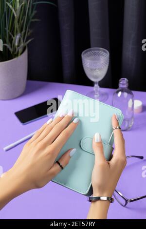 Womans hands holding notepad over violet table. Female summer accessories Stock Photo