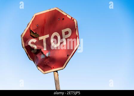 Damaged road sign stop covered with scratches and rusty. Rumpled road sign on a blue sky background. Stop sign with partly bent surface. Urban Grunge Stock Photo