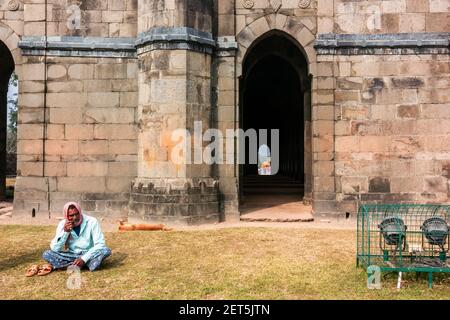 Malda, West Bengal, India - January 2018: An Indian man sitting outside the ancient Baroduari mosque in the village of Gaur. Stock Photo