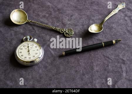 The vintage pocket clock, fountain pen, and spoons on the table Stock Photo