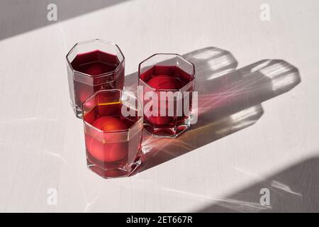 Three eggs in glasses of water is coloring with a natural food dyes of purple, pink, orange colors on a light background with shadows. Easter holiday Stock Photo