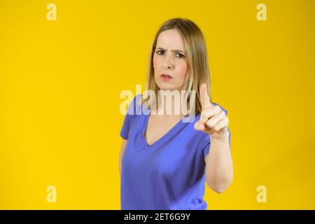 Young woman over isolated yellow background pointing finger to the camera with serious face Stock Photo