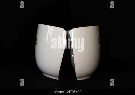 A closeup of a white coffee cup broken in half isolated on a black background Stock Photo
