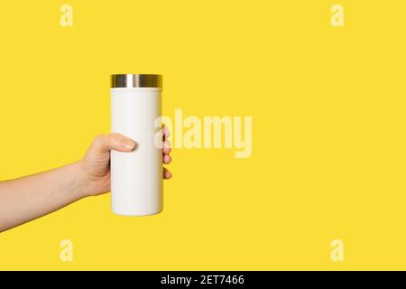 Hand holds white travel mug isolated on white background. Thermo cup or tumbler in female hand. Banner with copy space. Stock Photo