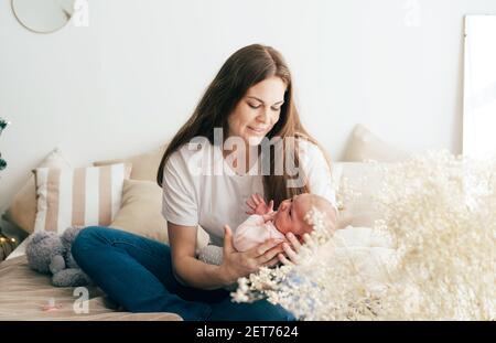 Young woman mother gently holds her newborn daughter. Lifestyle portrait family home life. Stock Photo