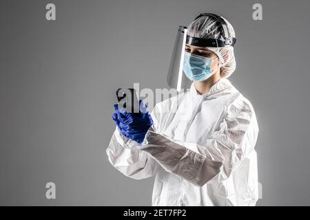 Woman doctor use phone wearing in hazmat protect for covid on gray background Stock Photo