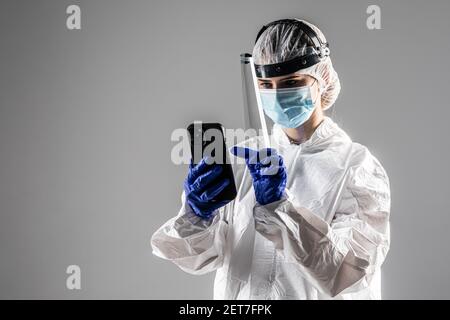 Woman doctor use phone wearing in hazmat protect for covid on gray background Stock Photo