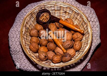 Wicker basket with walnuts and a wooden handled nutcracker with an open walnut. The base is made of crochet Stock Photo