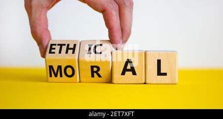Ethical or moral symbol. Businessman turns wooden cubes and changes the word 'moral' to 'ethical' on a beautiful yellow table, white background. Busin Stock Photo