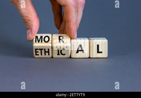 Ethical or moral symbol. Businessman turns wooden cubes and changes the word 'moral' to 'ethical' on a beautiful grey table, grey background. Business Stock Photo