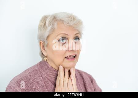 elderly woman with wide eyes and short hair holds her hands near the throat, sore throat health problems flu Stock Photo