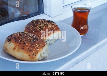 Close up Turkish pastry pogaca and black tea. Pastry food in white plate, breakfast snack. Stock Photo