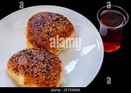 Close up Turkish pastry pogaca and tea on black background. Pastry food in white plate, breakfast snack. Stock Photo