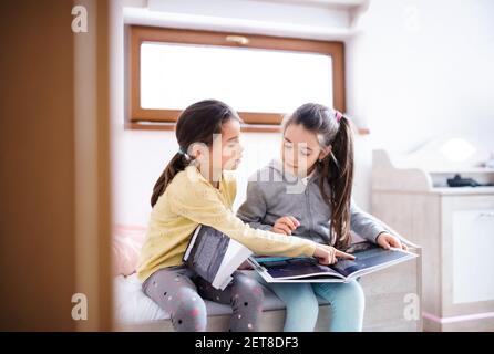 Two small girls sisters indoors at home, reading books. Stock Photo