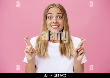 Optimistic hopeful energized girl with tanned skin and straight fair hair looing excited and happy at camera smiling with hope crossing fingers for Stock Photo