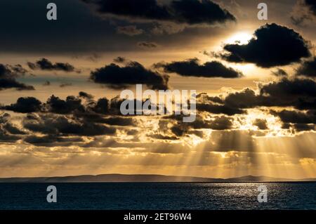 Sunbeams breaking through the clouds and lighting the waters of the Solent as the sun sets over the distant Isle of Purbeck as seen from Milford on Se Stock Photo