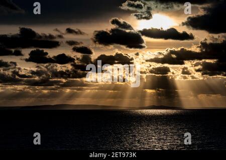 Sunbeams breaking through the clouds and lighting the waters of the Solent as the sun sets over the distant Isle of Purbeck as seen from Milford on Se Stock Photo