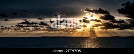 Sunbeams breaking through the clouds and lighting the waters of the Solent as the sun sets over the distant Isle of Purbeck as seen from Milford on Se Stock Photo