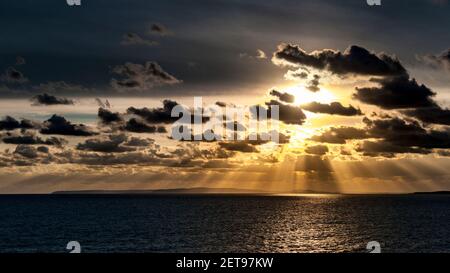 Sunbeams breaking through the clouds and lighting the waters of the Solent as the sun sets over the distant Isle of Purbeck as seen from Milford on Se Stock Photo