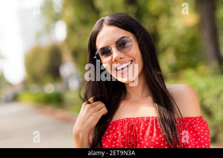 Photo portrait of beautiful brunette girl laughing in sunglass touching hair spending time in park in summer Stock Photo