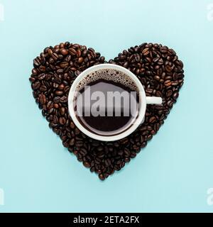 Coffee beans in shape of heart with white cup on blue background. Creative minimal coffee drink concept. Stock Photo