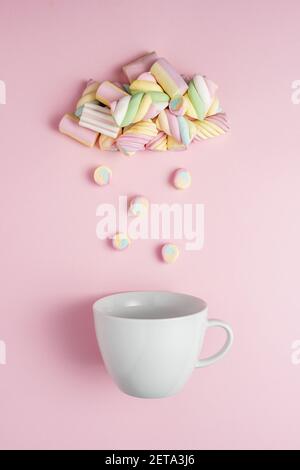 Marshmallows in shape of rainy cloud with white cup on pink background. Creative minimal sweet holiday food concept. Stock Photo