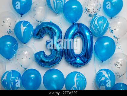 Blue number 30 celebration foil balloons with helium balloons on white background. Party decoration for happy birthday celebration. Stock Photo