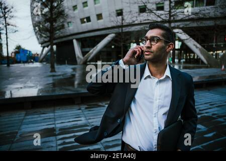 Young mixed race business man standing outside office talking on cellular device Stock Photo