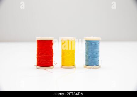 A closeup of red, yellow, and blue thread spools in the light background Stock Photo