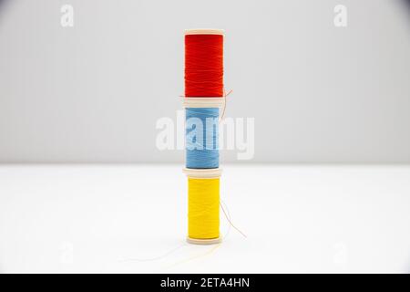 Three thread spools of red, blue, and yellow colors stacked on each other and isolated in the light background Stock Photo