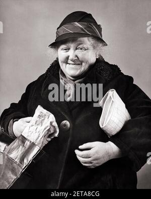 1930s 1940s POOR DEPRESSION ERA WOMAN SMILING LOOKING AT CAMERA WEARING WINTER COAT SCARF HAT HOLDING POCKET BOOK & SHOPPING BAG - c1872 HAR001 HARS FEMALES STUDIO SHOT POOR COPY SPACE HALF-LENGTH LADIES PERSONS CHARACTER SENIOR ADULT B&W EYE CONTACT SENIOR WOMAN HAPPINESS OLDSTERS CHEERFUL OLDSTER PRIDE OCCUPATIONS SMILES ELDERS JOYFUL JOLLY BLACK AND WHITE CAUCASIAN ETHNICITY ERA GREAT DEPRESSION HAR001 OLD FASHIONED Stock Photo