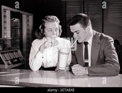 1950s TEENAGE SWEETHEARTS BOY GIRL SITTING AT SODA FOUNTAIN COUNTER DRINKING SHARING SINGLE MILKSHAKE WITH TWO STRAWS  - f6772 HAR001 HARS SHARING OLD TIME NOSTALGIA OLD FASHION 1 JUVENILE MILKSHAKE BALANCE TEAMWORK STRONG JOY LIFESTYLE CELEBRATION FEMALES HEALTHINESS COPY SPACE FRIENDSHIP HALF-LENGTH PERSONS CARING MALES TEENAGE GIRL TEENAGE BOY SERENITY CONFIDENCE STRAWS B&W DATING TEMPTATION HAPPINESS WELLNESS HEAD AND SHOULDERS CHOICE EXCITEMENT RECREATION AT CONNECTION CONCEPTUAL STYLISH TEENAGED PERSONAL ATTACHMENT SWEETHEARTS AFFECTION EMOTION GROWTH JUVENILES TOGETHERNESS Stock Photo