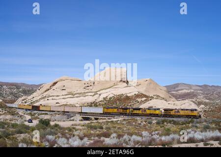 Union Pacific Railroad train traveling through the Mojave Desert shown against the Mormon Rocks in the Cajon Pass.. Stock Photo