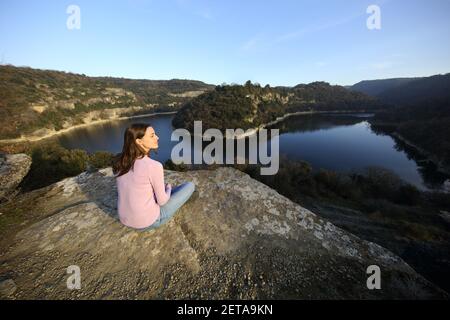 Relaxed woman sitting contemplating nature beside a river in the mountain Stock Photo