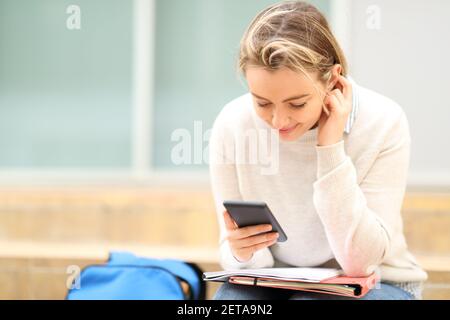Student checking smart phone sitting in stairs in the street Stock Photo