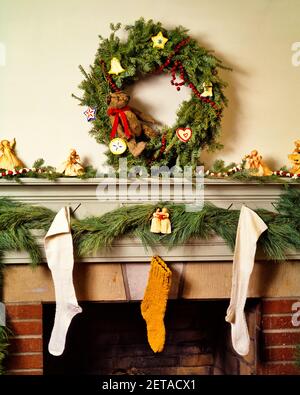 1980s CHRISTMAS FIREPLACE MANTLE DECORATED WITH HOMESPUN HAND CRAFTED ITEMS WREATH GARLAND STOCKINGS ORNAMENTS - kx10205 TEU001 HARS CHIMNEY OLD FASHIONED Stock Photo