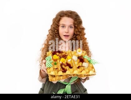 beautiful red-haired teenager girl with wavy afro curls holding homemade Easter basket with toy chickens and eggs in studio on white background. Close Stock Photo