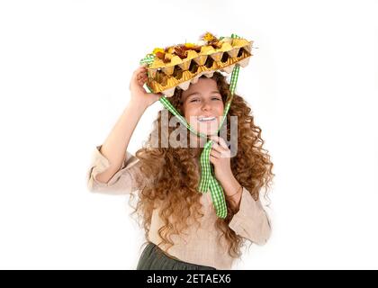 Creative beautiful teenage girl with curly red hair put carton basket with Easter decorations eggs as hat on head, cheerfully in studio on white backg Stock Photo
