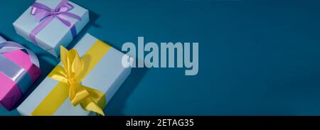 Gift boxes with different colors on a banner template. Blue gift box and yellow bow against bold blue background. Stock Photo
