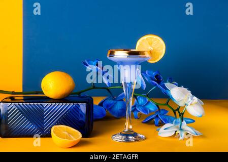 Tropical cocktail in glass with fresh lemon decor, blue orchid flower, glass texture podium on yellow and blue background. Trendy minimalism geometric Stock Photo