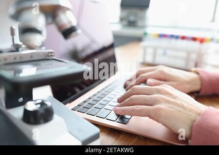 Female hands are working on laptop next to microscope Stock Photo