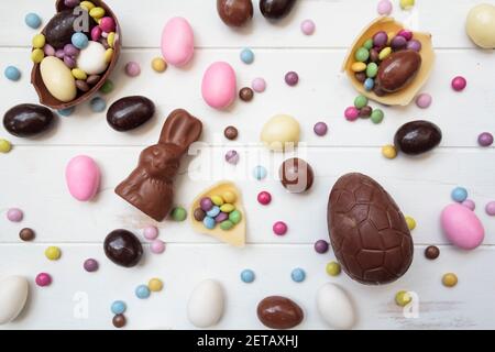 Top view of large variety of easter sweets, chocolate eggs, chocolate bunny, sweet almonds and other candies on white wooden table Stock Photo