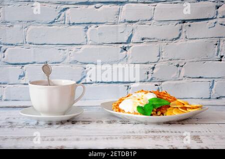 A delicious breakfast, a cup of black tea and a plate of waffles, cream and banana pieces are on the table. Close-up. Stock Photo