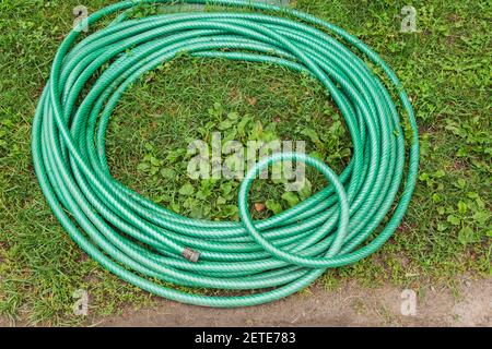Coiled green rubber garden watering hose with brass male shank on grass lawn Stock Photo