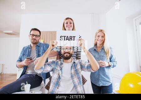 A group of joyful and young engineers is announcing the start of their new project by showing off the paper with 'start' written on it in a big bright Stock Photo