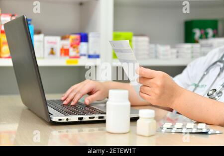 Pharmacist using the computer laptop in chemist shop or pharmacy drug store. Hand holding medicine and key the prescription order. Stock Photo