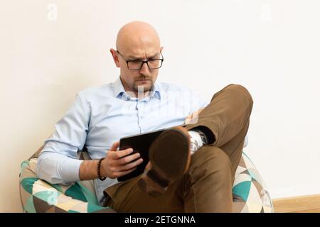 middle-aged man using tablet computer while sitting on chair bag Stock Photo