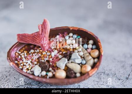 Half a chocolate egg filled with popped rice. The egg is decorated with multicolored precious stones and a mermaids tail Stock Photo