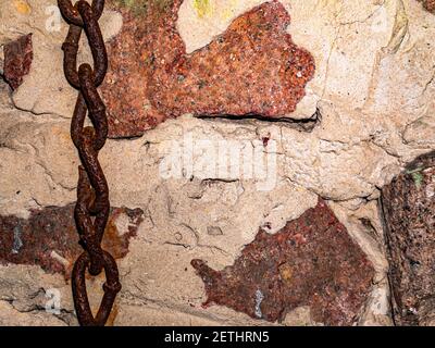 Old rusty iron chain on the background of a granite wall. Links of a metal chain. Grant wall. Granite stones. Cement masonry. Background image. Place Stock Photo