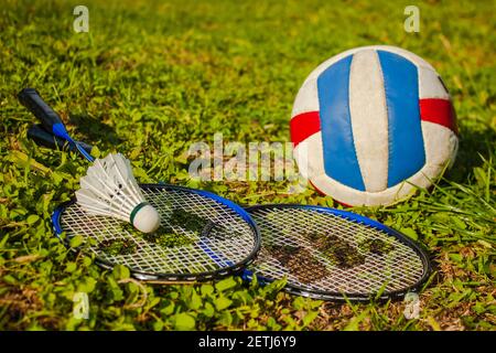 A volleyball ball, badminton rackets and a shuttlecock lie on the grass. The concept of outdoor sports games Stock Photo